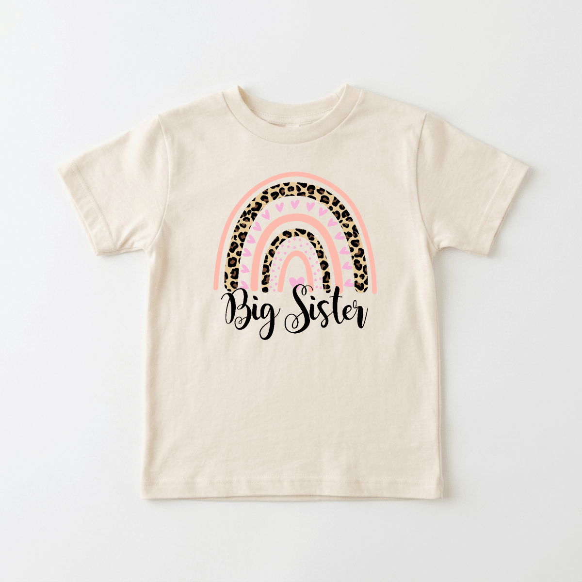 The Toodleroos Big Sister Toddler Shirt features a cream color with a charming rainbow design in pink, tan, and leopard print patterns. “Big Sister” is written below the rainbow in an elegant black script font, making this shirt the perfect choice for a special pregnancy announcement or to celebrate your growing family with your little one.
