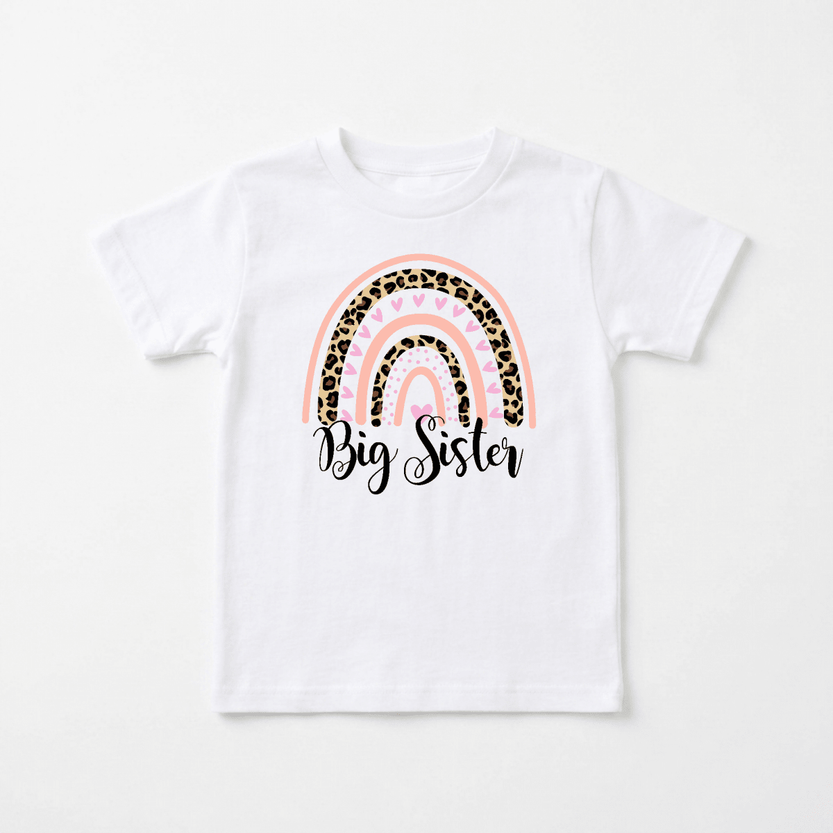 The Big Sister Toddler Shirt – Leopard Rainbow Design by Toodleroos features a white tee adorned with a pink, gold, and leopard print rainbow. The phrase “Big Sister” is written in elegant black cursive beneath the rainbow, creating an adorable top that’s perfect for big sister announcements or pregnancy reveals.