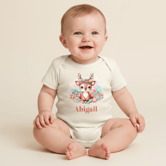 A happy baby sits wearing the Toodleroos Custom Candy Deer Baby Onesie, featuring a charming deer illustration, vibrant floral accents, and the name Abigail personalized on the front—an ideal custom baby shower gift.