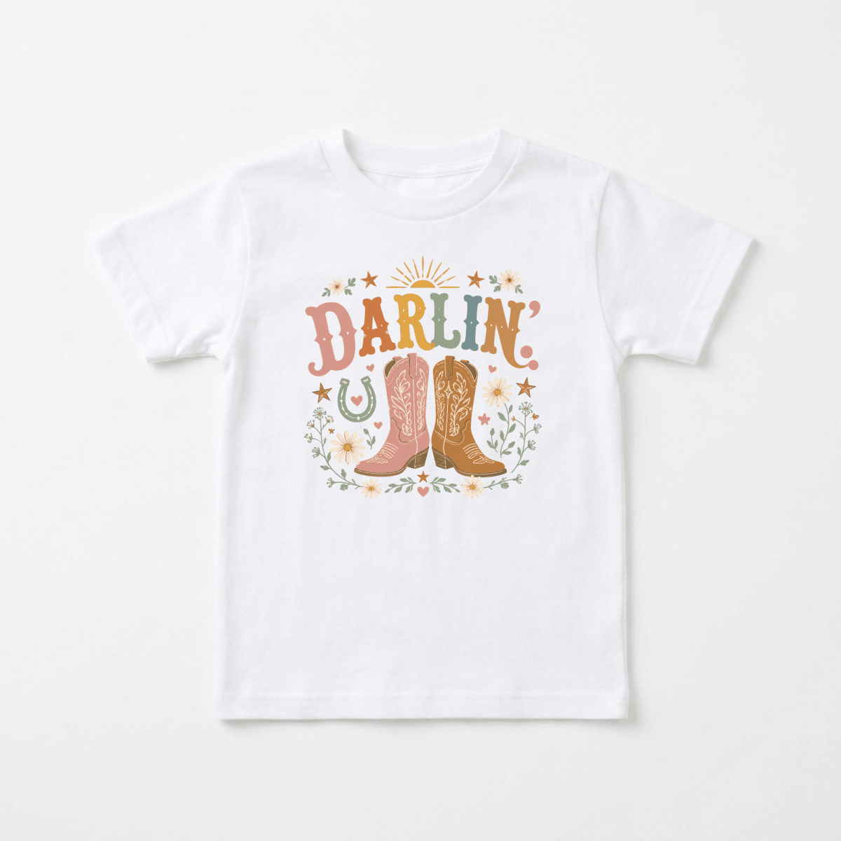 Dress your little one for western adventures with the Toddler Cowgirl Shirt – Darlin’ Western Cowboy Boots Short-Sleeve Tee from Toodleroos. This adorable tee features “Darlin’” in colorful letters above a pair of pink and brown cowboy boots, surrounded by pastel flowers, stars, a horseshoe, and leaves—perfect for any toddler cowgirl!.