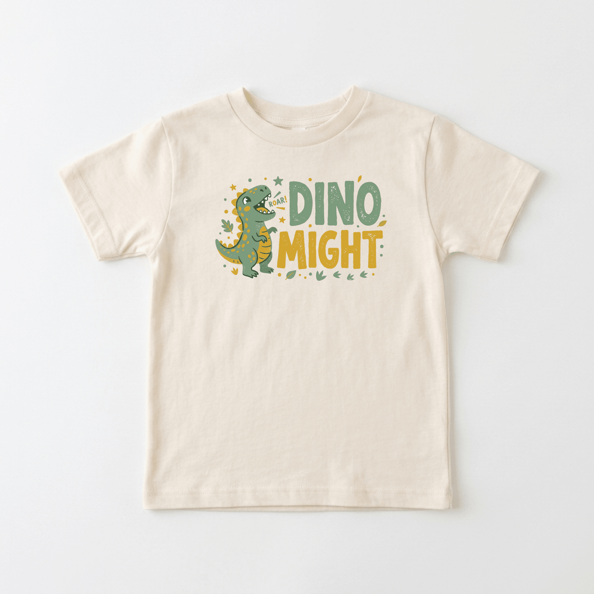 The Toodleroos Dino Might Toddler Shirt – Roaring Dinosaur Tee is a cream-colored t-shirt showcasing a playful green cartoon dinosaur surrounded by stars and leaves, with “DINO MIGHT” boldly displayed in green and yellow letters on the front. This lively dinosaur shirt is an ideal birthday gift or a fun tee for any little dino lover.