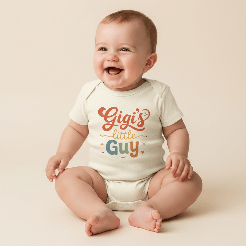A smiling baby sits on a neutral background, dressed in the Toodleroos Gigi Baby Onesie – Gigi’s Little Guy Grandson Short-Sleeve Bodysuit featuring “Gigi’s little Guy” in orange, yellow, and blue letters with charming stars and hearts—the perfect grandson bodysuit and a thoughtful gift from grandma.