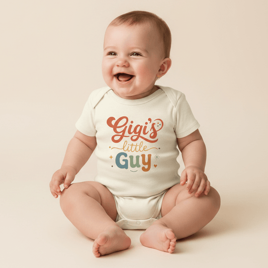 A smiling baby sits on a neutral background, dressed in the Toodleroos Gigi Baby Onesie – Gigi’s Little Guy Grandson Short-Sleeve Bodysuit featuring “Gigi’s little Guy” in orange, yellow, and blue letters with charming stars and hearts—the perfect grandson bodysuit and a thoughtful gift from grandma.