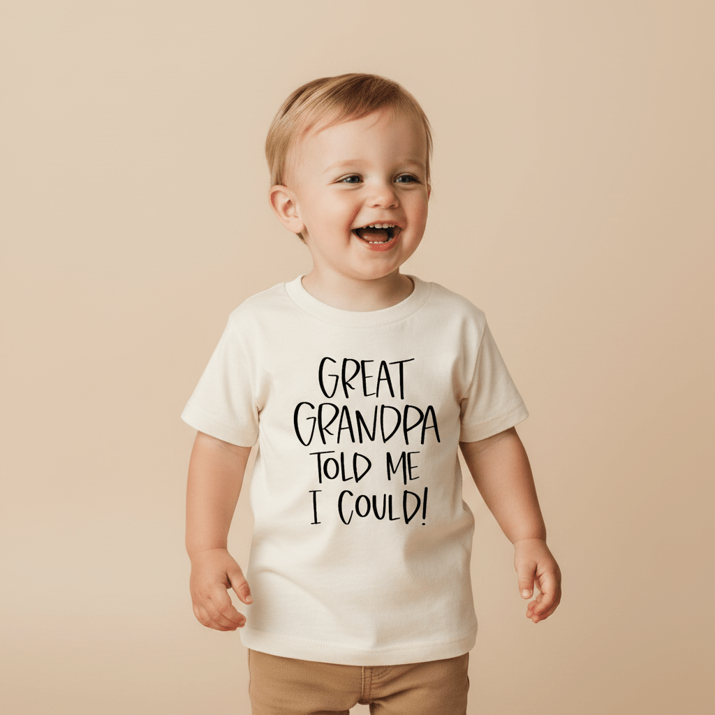 A smiling toddler wears the Toodleroos Great Grandpa Told Me I Could Toddler Shirt – Funny Family Tee in cream, standing against a neutral background—an adorable choice and the perfect great-grandpa gift.