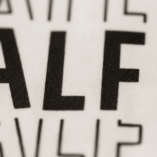 Close-up of bold black “ALF” text on a white fabric, part of the Toodleroos Half Birthday Kids Shirt – 6 Month Milestone Tee. Partial letters are visible at the edges, highlighting the playful black and white design that’s perfect for milestone photos or celebrating a fun half birthday.