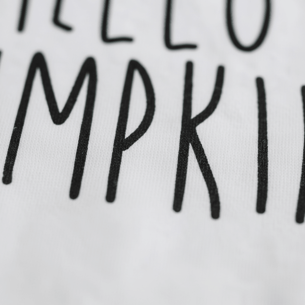 A close-up of black text reading “Hello Pumpkin” in tall, handwritten-style letters on white fabric—an adorable detail from the Toodleroos Hello Pumpkin Onesie – Baby Fall Bodysuit, perfect for celebrating autumn with your little one.