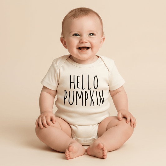 A smiling baby sits against a neutral background, dressed in the Toodleroos Hello Pumpkin Onesie – Baby Fall Bodysuit, featuring bold black “HELLO PUMPKIN” lettering on the front—an adorable and cozy fall outfit perfect for autumn days.