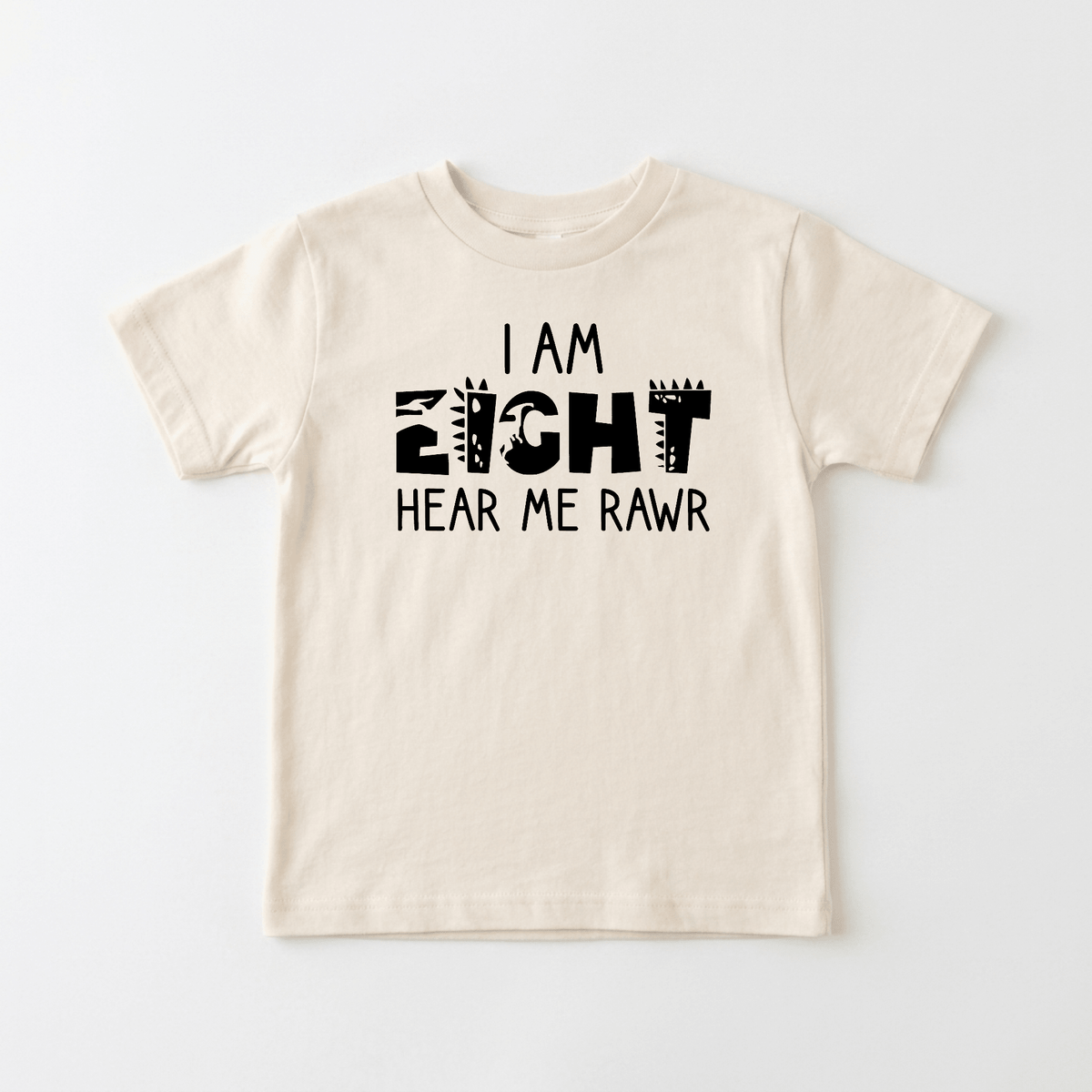 A beige “I Am Eight Hear Me Rawr Kids Shirt – Dinosaur 8th Birthday Tee” by Toodleroos, featuring playful black lettering with animal print and spikes—perfect for any little dino fan celebrating their 8th birthday.