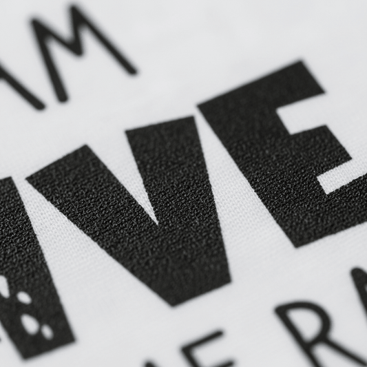 Close-up of bold, black, partially visible letters VE printed on white textured fabric from the “I Am Five Hear Me Rawr Kids Shirt – Dinosaur 5th Birthday Tee” by Toodleroos. The image captures the fine fabric details and sharp edges of the letters, highlighting the quality you’d want in a special dinosaur birthday shirt for kids.