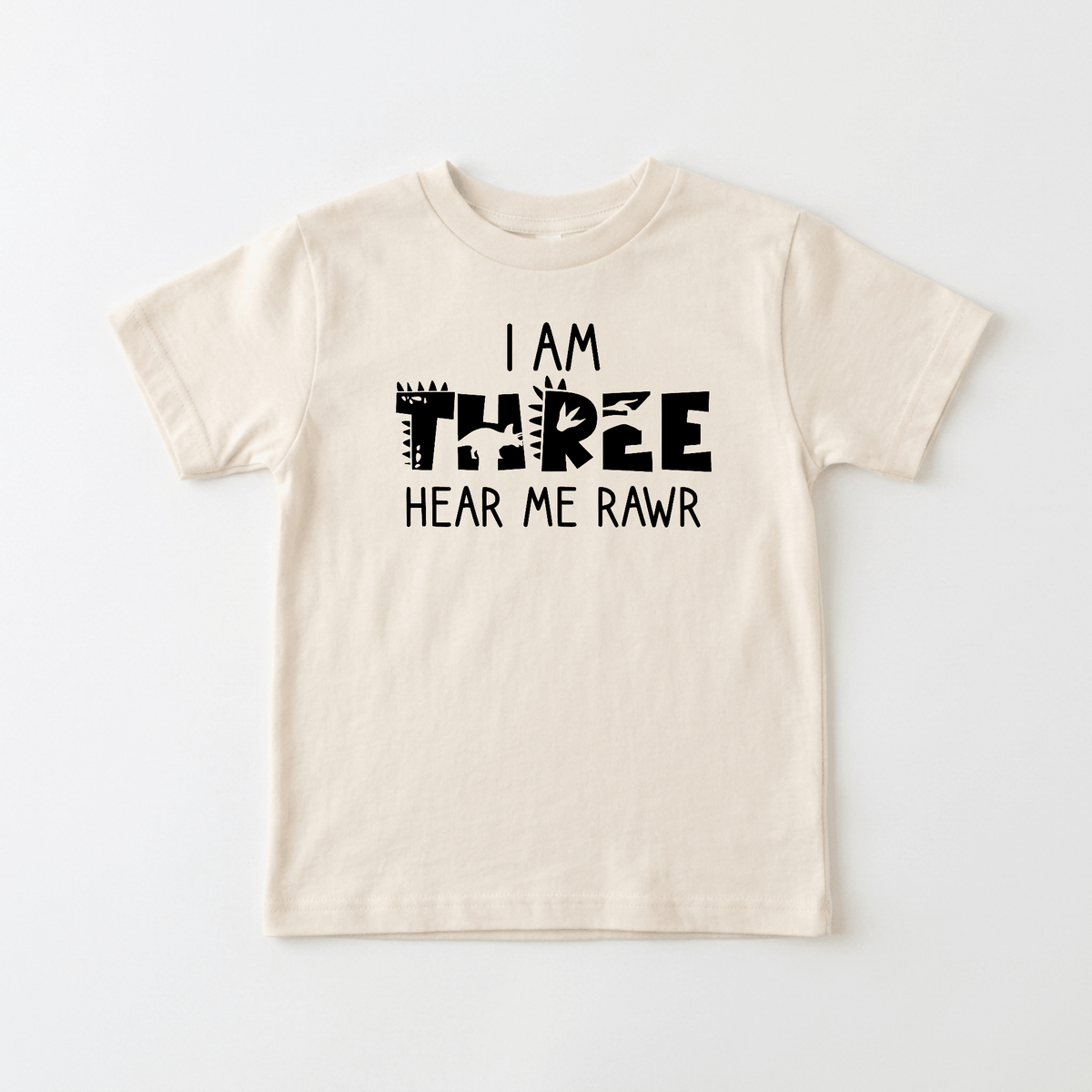 Celebrate your little one’s big day with the Toodleroos “I Am Three Hear Me Rawr Toddler Shirt – Dinosaur 3rd Birthday Tee”—a beige children’s t-shirt featuring playful black lettering and an animal-patterned “three,” making it the perfect dino-themed birthday shirt for turning three.