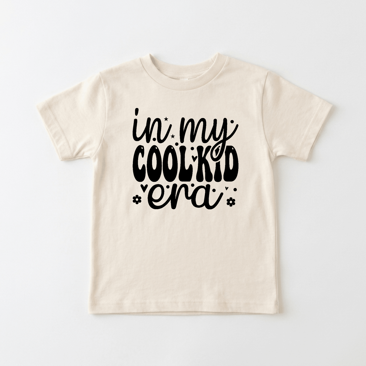 Dress your child in the Toodleroos In My Cool Kid Era Kids Shirt – Trendy Retro Tee, a beige t-shirt featuring bold, playful black lettering that reads “In My Cool Kid Era,” accented with charming star and flower doodles—perfect for fans of funny kids shirts who love a touch of humor and retro flair.