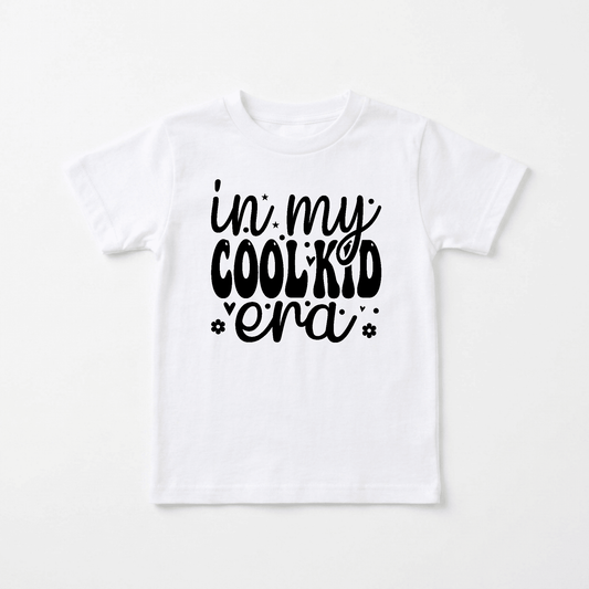 Introducing the In My Cool Kid Era Kids Shirt – Trendy Retro Tee by Toodleroos: a white shirt featuring playful black text that reads “in my COOL KID era” in mixed fonts, surrounded by small stars and flowers. This retro-inspired tee blends nostalgic style with a modern twist, making it perfect for any kid who loves funny shirts and standout fashion.