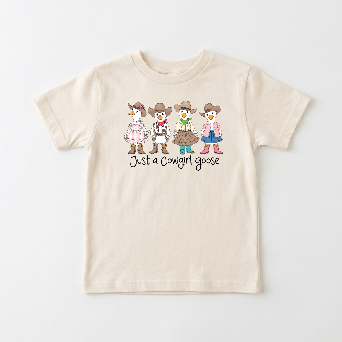 The Toodleroos Just a Cowgirl Goose Toddler Girls Shirt is a beige western tee featuring four cartoon geese dressed in cowgirl outfits and hats above the phrase “Just a Cowgirl Goose.” This cute shirt is perfect for toddlers who love country style or want an adorable cowgirl-themed top for any occasion.