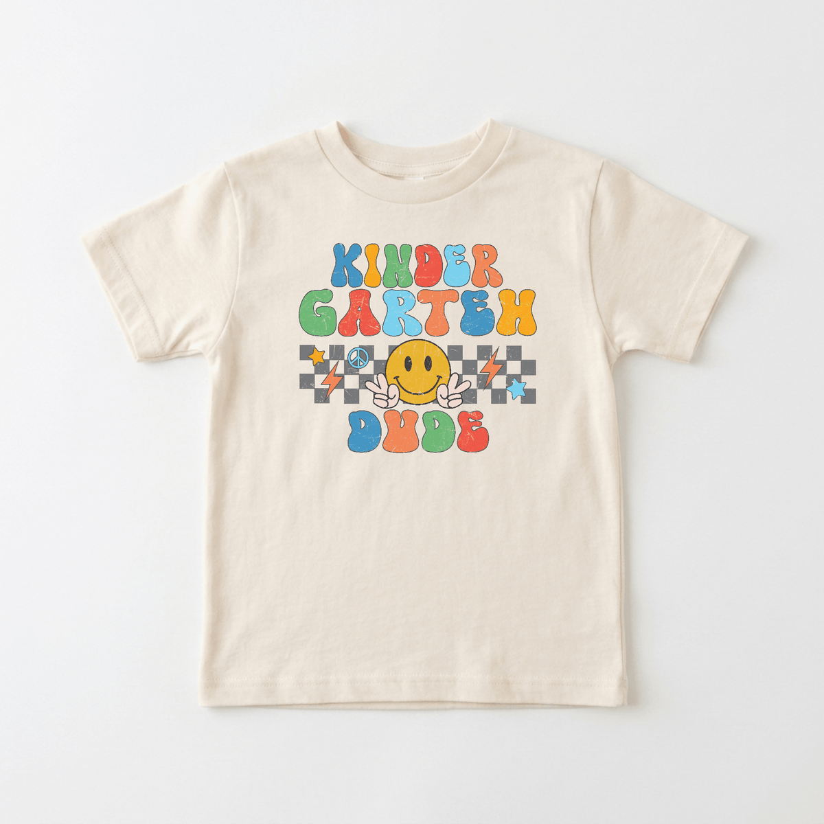 The Kindergarten Dude Youth Shirt – Retro Back to School Tee by Toodleroos features a beige design with colorful “Kinder Garten Dude” text, a cheerful yellow smiling face with hands, and a backdrop of black, white, and vibrant stars and squares—making it the perfect retro first day of kindergarten or back-to-school shirt.