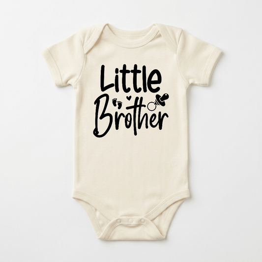 Dress your little one in the Toodleroos Little Brother Baby Onesie – Hand-Lettered Sibling Design, a soft cream-colored bodysuit adorned with “Little Brother” in bold black lettering, charming baby footprints, and a cute pacifier illustration. This cozy outfit is perfect as a coming home ensemble for your newest addition.