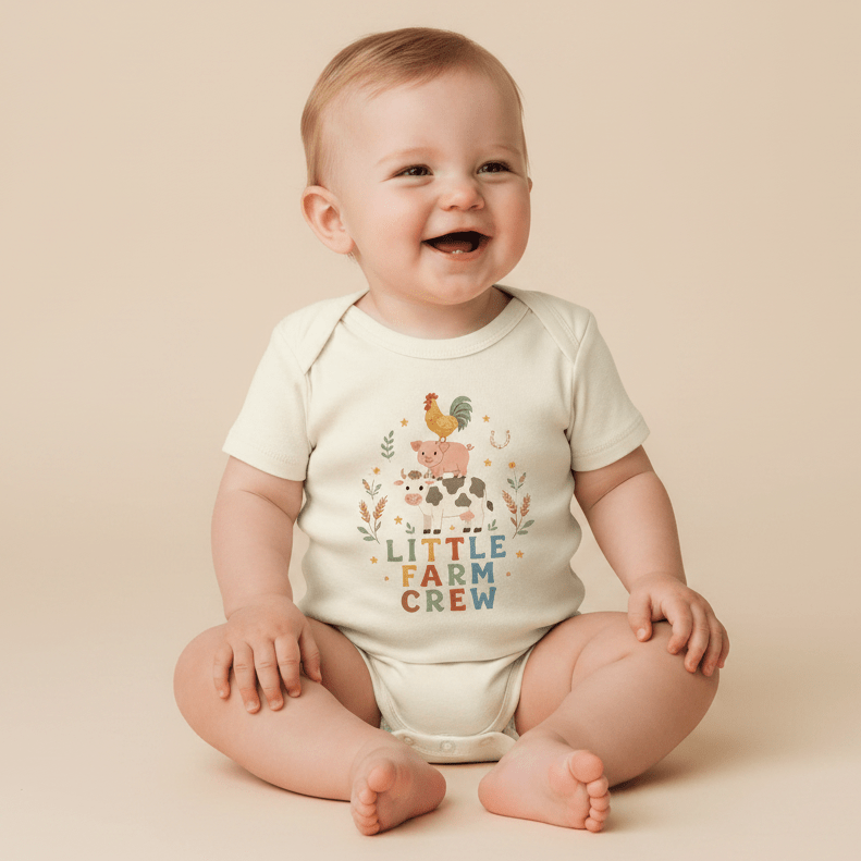 A smiling baby in a white onesie sits on a beige background. The Toodleroos Little Farm Crew Farm Animal Baby Onesie showcases a vibrant farm animal graphic with “Little Farm Crew” printed underneath, bringing extra country charm to this delightful baby bodysuit.