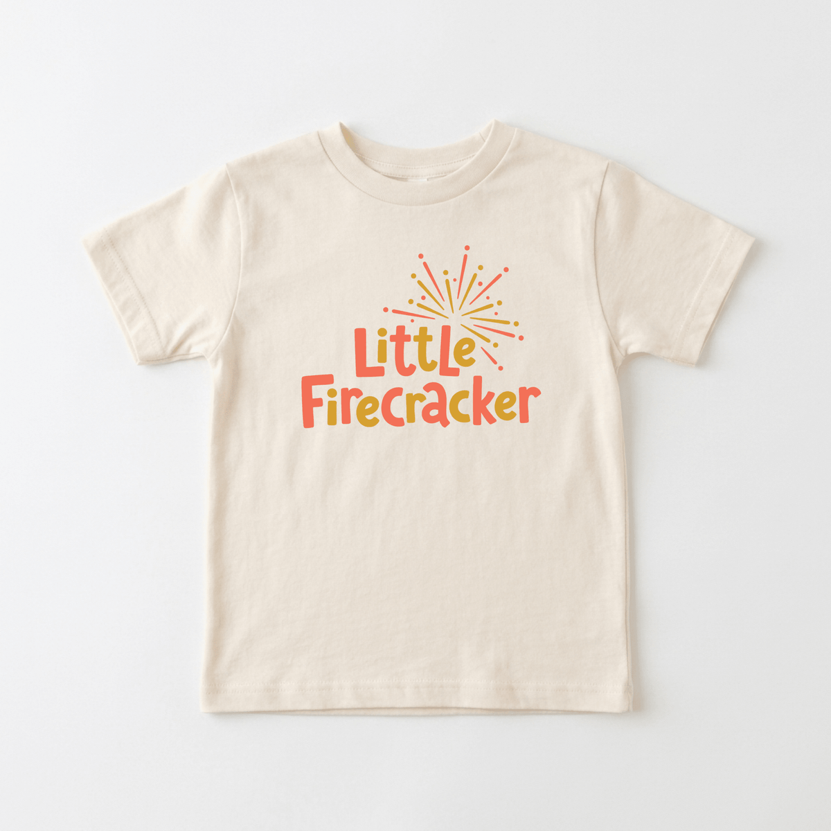 The Toodleroos Little Firecracker 4th of July Toddler Shirt features a beige children’s t-shirt with “Little FireCracker” printed in bold orange and red lettering beneath a vibrant yellow and orange firework graphic on the chest. Displayed on a plain white background, this festive firework tee is perfect for patriotic celebrations as a 4th of July toddler shirt.
