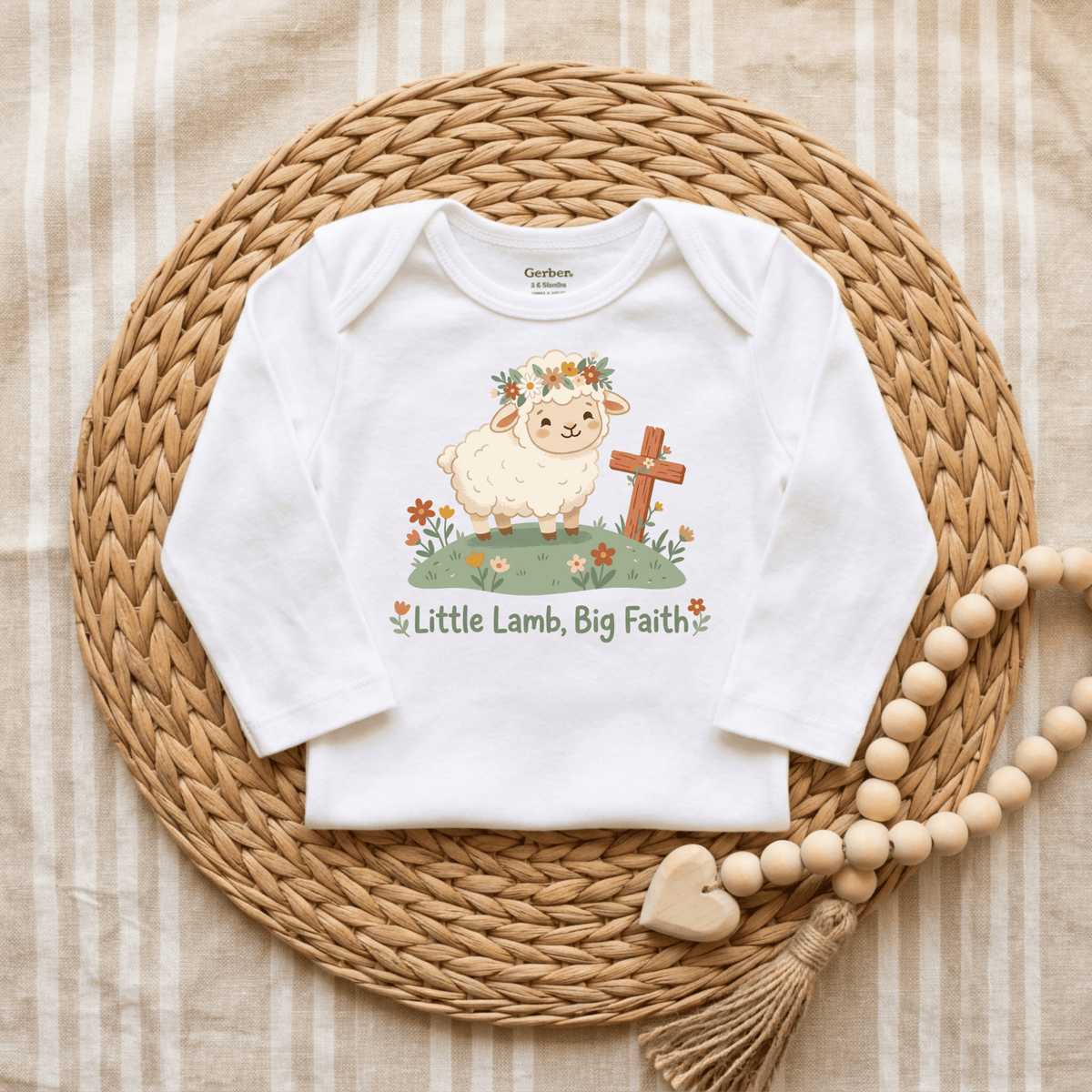 The Toodleroos Little Lamb Big Faith Onesie – Baby Girl Faith Bodysuit features a charming cartoon lamb, flowers, a cross, and the words “Little Lamb, Big Faith,” displayed on a woven mat with wooden beads and a striped fabric background—making it the perfect faith-themed baby gift or adorable baby baptism onesie.