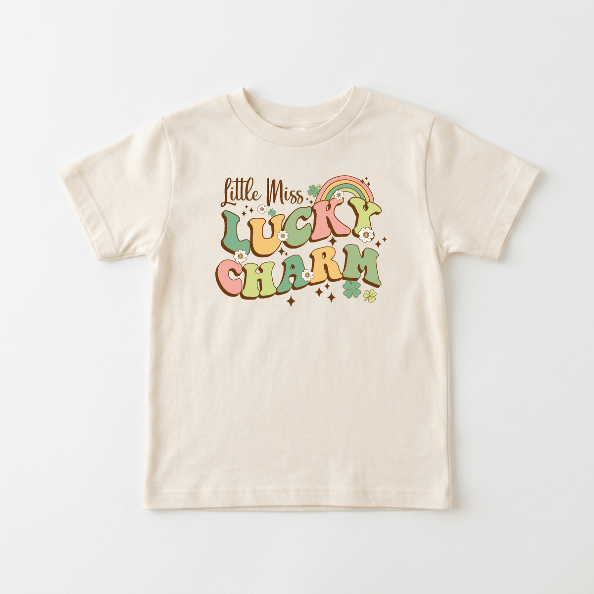 Introducing the Little Miss Lucky Charm Toddler Girls Shirt by Toodleroos—a beige St. Patrick’s Day tee featuring vibrant retro text, a rainbow, stars, and clovers. Laid flat on a white background, this pastel rainbow toddler shirt is the perfect outfit for your lucky little one!.
