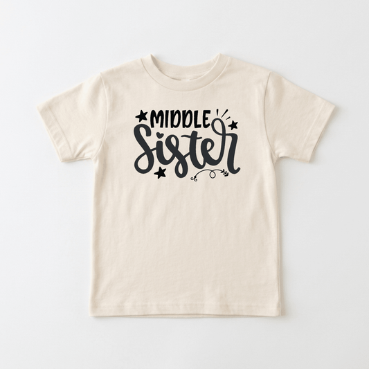 The Toodleroos Middle Sister Toddler Shirt features a fun, hand-lettered “Middle Sister” design in bold black lettering with whimsical stars and swirls, making it the perfect sibling gift or adorable shirt for any toddler.