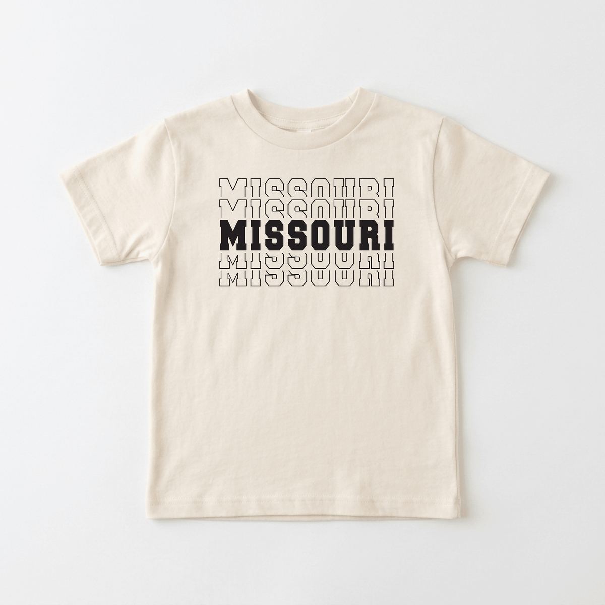 The Missouri Varsity Kids Shirt – State Pride Tee by Toodleroos features “MISSOURI” repeated three times in outlined black letters across a beige t-shirt, with the middle word bolded and filled in for emphasis—a stylish way for little ones to show off their Show-Me State pride.