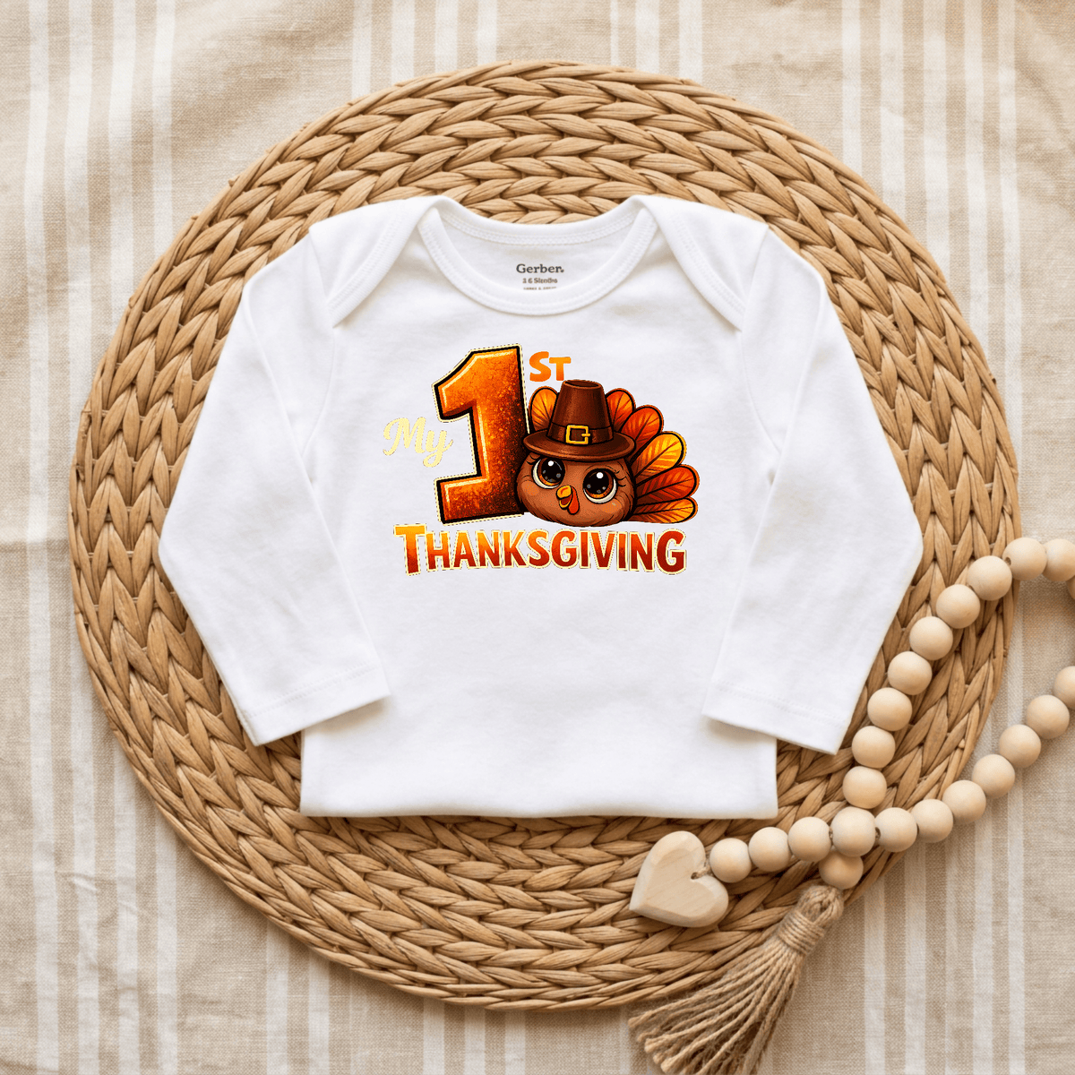 The Toodleroos My 1st Thanksgiving Onesie – Baby Turkey Bodysuit is a white Gerber bodysuit featuring “My 1st Thanksgiving” and an adorable cartoon turkey in a pilgrim hat, displayed on a woven placemat with a beaded heart accent—making it the perfect Thanksgiving baby outfit for your little one’s special celebration.