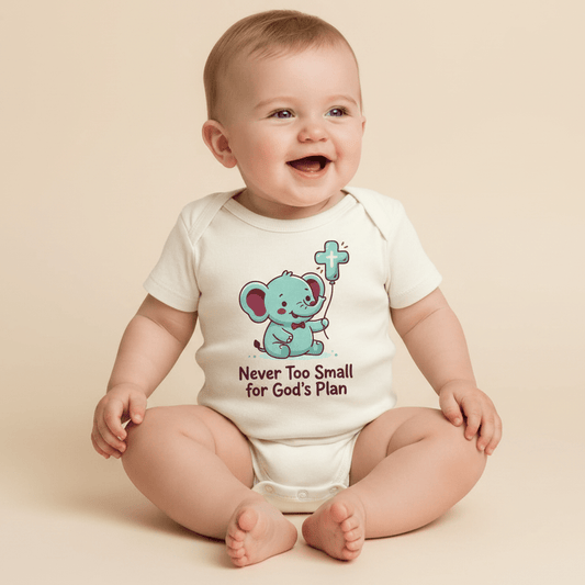 A smiling baby sits in a white Toodleroos Never Too Small for God’s Plan Onesie – Faith Bodysuit, featuring an adorable illustration of an elephant holding a cross and the phrase “Never Too Small for God’s Plan”—a perfect baptism gift and piece of faith-inspired baby clothing.
