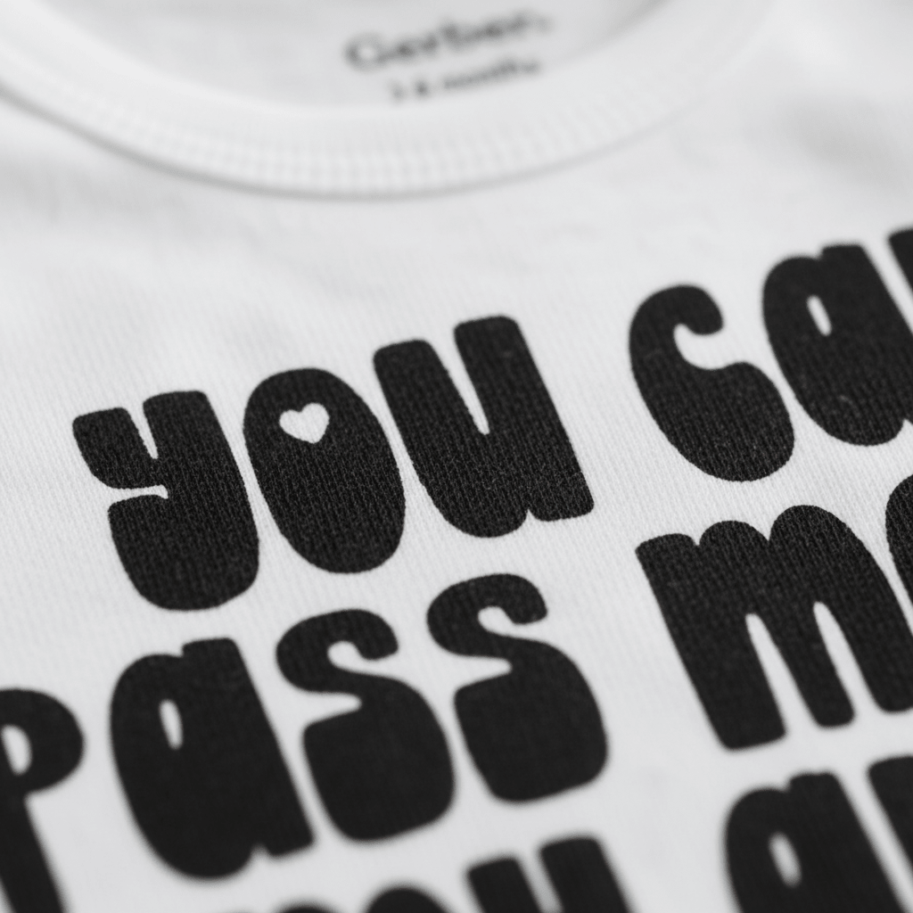 Close-up of the Toodleroos Pass Me to My Aunt Now Baby Onesie—a white, gender-neutral bodysuit with bold black text reading “pass me to my aunt now” in playful lettering. The design features a small heart shape inside the letter ‘o’, making this funny aunt bodysuit a charming baby shower gift.
