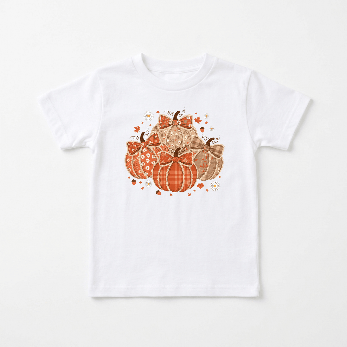 Introducing the Patchwork Pumpkin Toddler Girls Shirt – Fall Floral Tee from Toodleroos. This white shirt features a charming graphic of five patterned pumpkins in orange and brown hues, accented with small stars and sparkles. The central pumpkin is adorned with a cute bow, making this handmade farmhouse-inspired tee the ideal choice for cozy autumn days or as a standout outfit for your little one’s fall family photoshoot.