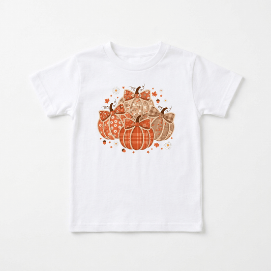 Introducing the Patchwork Pumpkin Toddler Girls Shirt – Fall Floral Tee from Toodleroos. This white shirt features a charming graphic of five patterned pumpkins in orange and brown hues, accented with small stars and sparkles. The central pumpkin is adorned with a cute bow, making this handmade farmhouse-inspired tee the ideal choice for cozy autumn days or as a standout outfit for your little one’s fall family photoshoot.