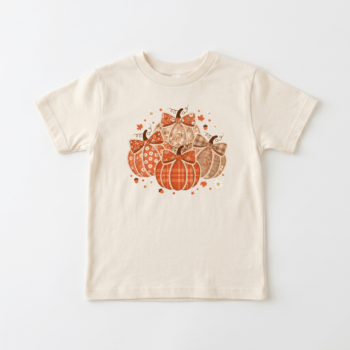 The Toodleroos Patchwork Pumpkin Toddler Girls Shirt – Fall Floral Tee is a beige top adorned with a cluster of orange and brown decorative pumpkins featuring floral and patterned designs, surrounded by small stars and leaves—perfect as a handmade farmhouse fall shirt or a sweet outfit for your next family photoshoot.