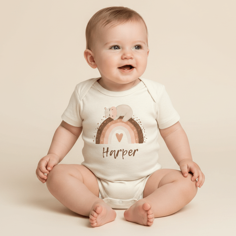 A smiling baby sits on a light background, wearing the Toodleroos Personalized Bear Rainbow Baby Onesie – a custom name bodysuit adorned with cheerful heart and bear designs. This boho-inspired onesie, personalized here with the name Harper, makes a wonderful baby gift.
