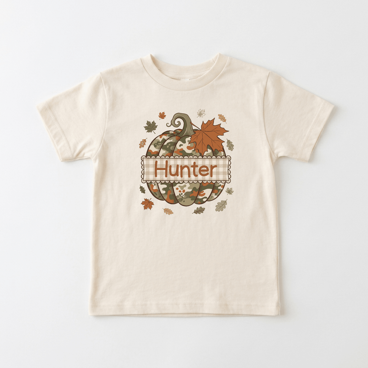 Introducing the Personalized Camo Pumpkin Toddler Shirt – Fall Name Tee by Toodleroos: a beige toddler tee featuring a camouflage pumpkin surrounded by autumn leaves and customized with your child’s name—perfect for boys who love fall!.