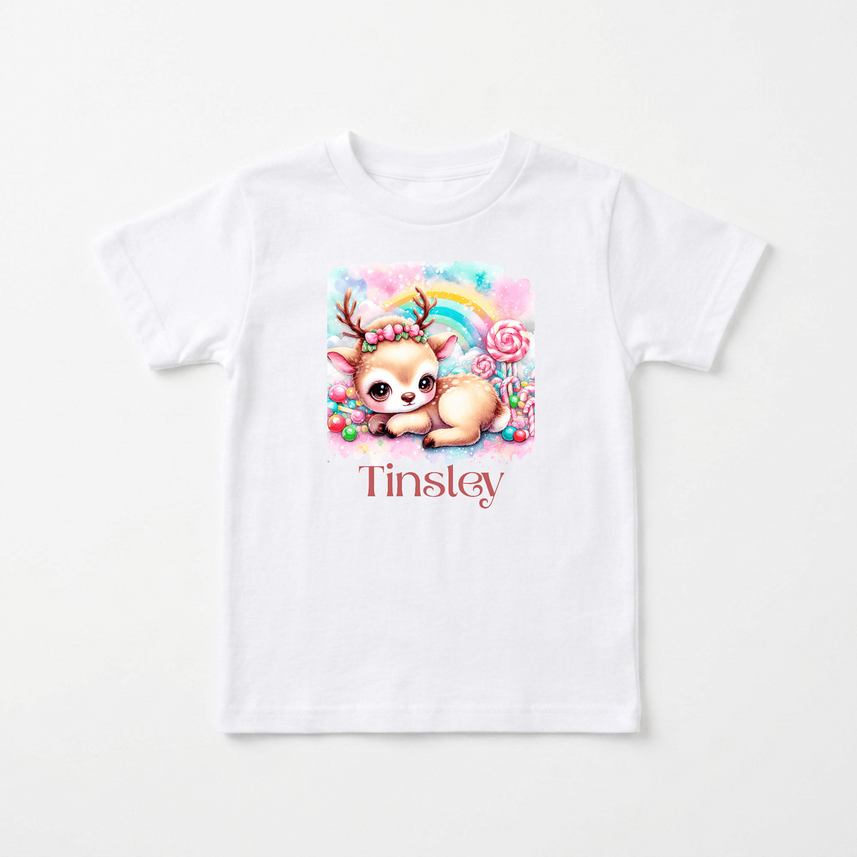 Introducing the Personalized Candy Deer Toddler T-Shirt – Custom Name Tee by Toodleroos! This adorable white t-shirt features a cute cartoon baby deer, colorful candy, and a pastel rainbow. Your child’s name, such as “Tinsley,” is printed in bold red beneath the illustration for a charming personalized touch—making it the perfect toddler tee.