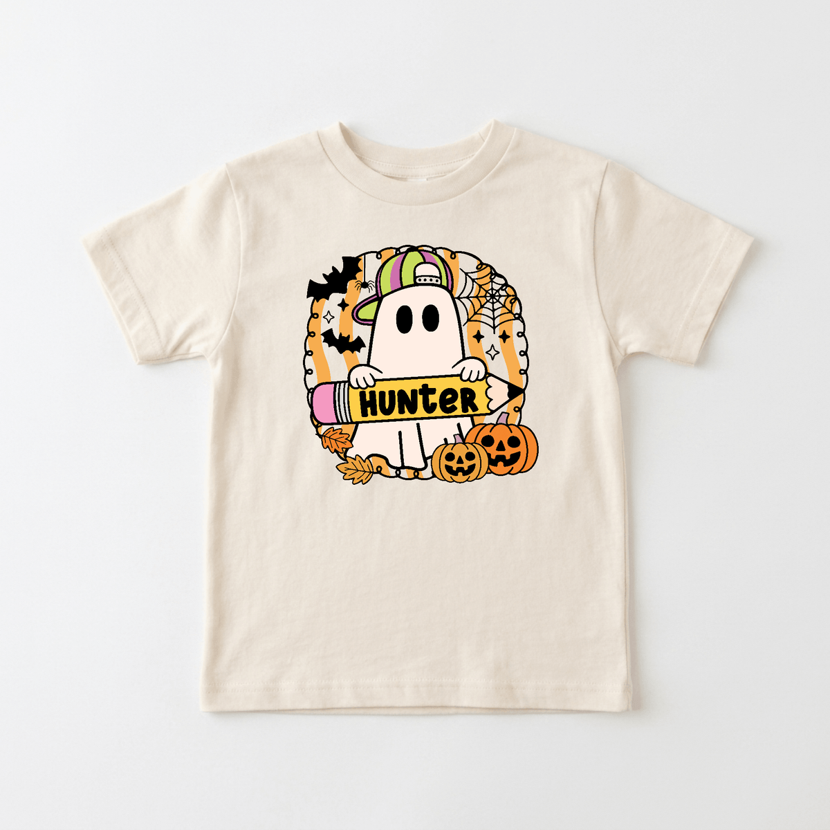 Dress your little one in spooky season style with the Personalized Halloween Ghost Kids Shirt – Custom Name Tee from Toodleroos! This beige t-shirt features a cartoon ghost wearing a cap and holding a crayon labeled with your child’s name, surrounded by bats, pumpkins, autumn leaves, and spiderwebs for a festive Halloween-themed design. Perfect for kids who love Halloween fun, this personalized tee makes an adorable custom ghost shirt for the holiday!.