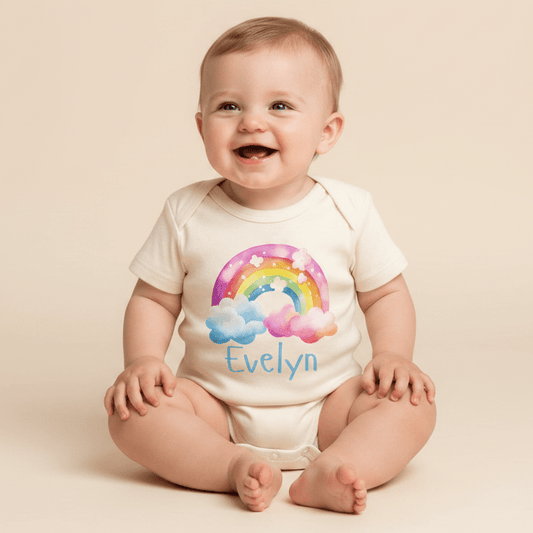 A happy baby sits wearing the Toodleroos Personalized Rainbow Cloud Baby Girl Onesie – Custom Name Bodysuit, featuring a cheerful rainbow and cloud design with “Evelyn” printed on the front—a perfect, thoughtful gift for baby showers.