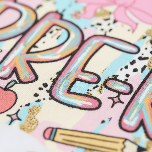 Featuring colorful, hand-drawn letters with a rainbow gradient style, this Toodleroos Pre-K Youth Tee – Bow & Apple Back to School Shirt is adorned with playful doodles like apples, pencils, and bows on a soft pastel background. With the bold “PE” partially displayed in outlined text, it’s perfect for a fun Pre-K shirt or as a standout first day of school outfit.