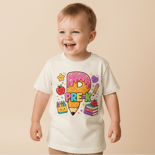 Dressed in the Toodleroos Pre-K Kids Shirt – Back to School Tee, this smiling toddler sports a white T-shirt featuring colorful Pre-K text, a playful cartoon pencil, donut, books, crayons, apple, and stars—the perfect first day of school outfit for little learners! This adorable Toodleroos tee is an ideal addition to any back to school shirts collection.