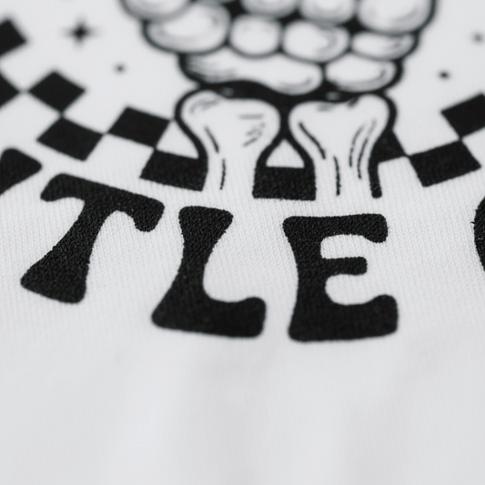 The Pretty Fly for a Little Guy Kids Shirt by Toodleroos features a black and white close-up design with bold “TLE” lettering and part of a stylized rock skeleton graphic, possibly including bones and checkered pattern details—making it the perfect retro kids shirt for your cool little one.