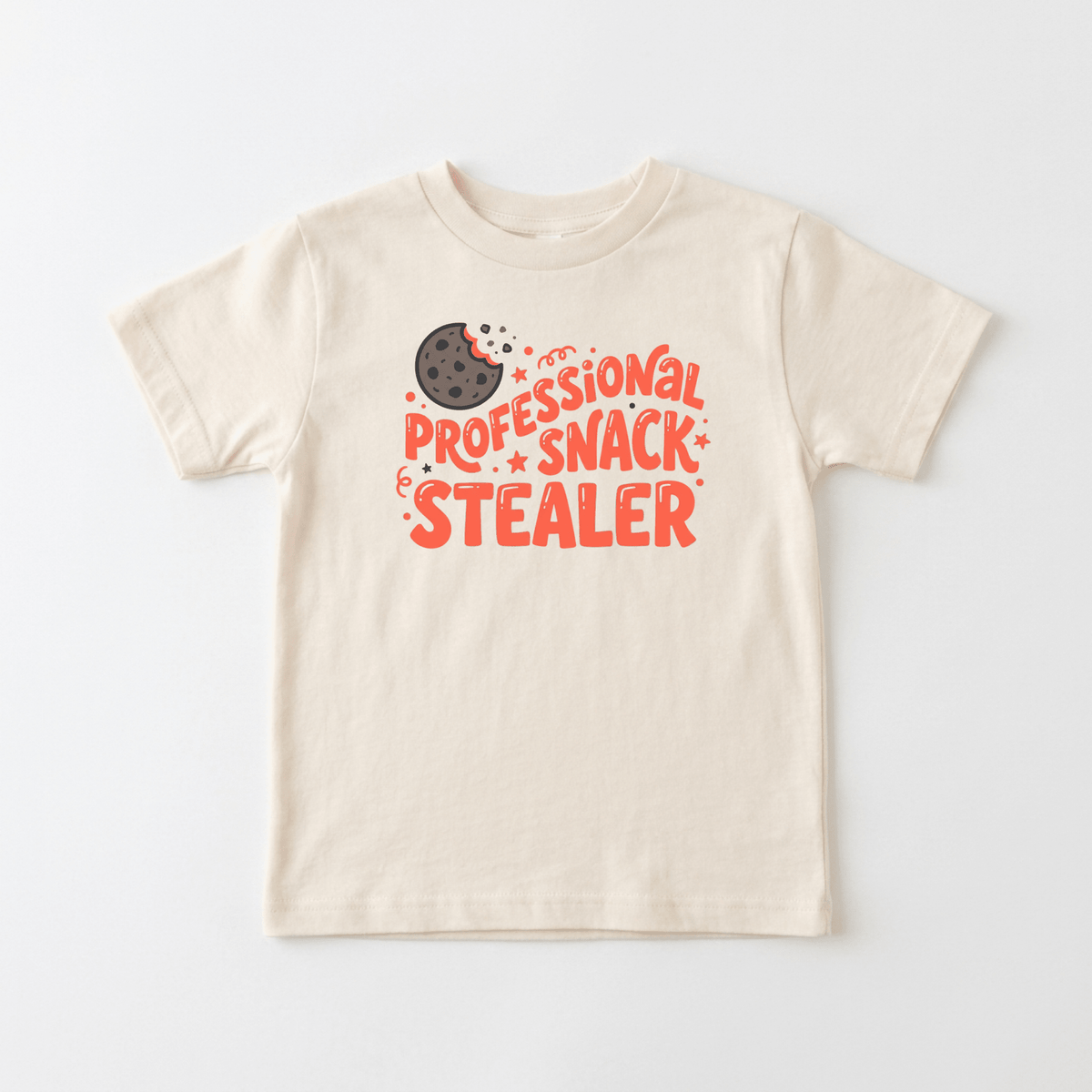 The Toodleroos Professional Snack Stealer Toddler Shirt – Funny Cookie Tee features a playful beige design with a bitten chocolate chip cookie and bold red text that reads “Professional Snack Stealer.” Laid flat on a white background, this toddler tee makes the perfect funny shirt for little ones who love their snacks.