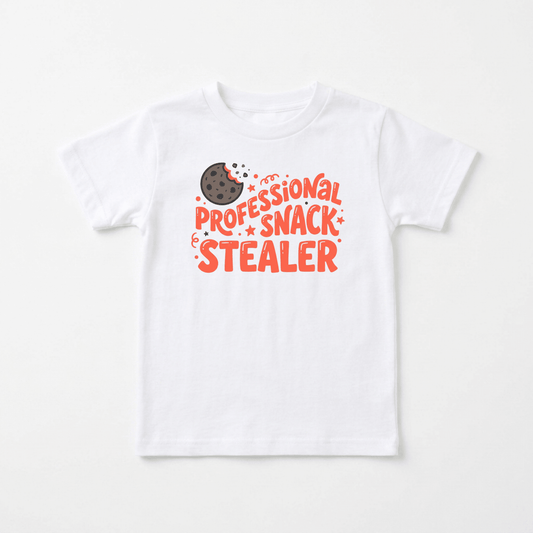 Dress your little mischief-maker in the Toodleroos Professional Snack Stealer Toddler Shirt – a funny cookie tee featuring a playful illustration of a bitten chocolate chip cookie and bold orange and red “Professional Snack Stealer” lettering. This adorable graphic tee is perfect for snack-loving toddlers!.