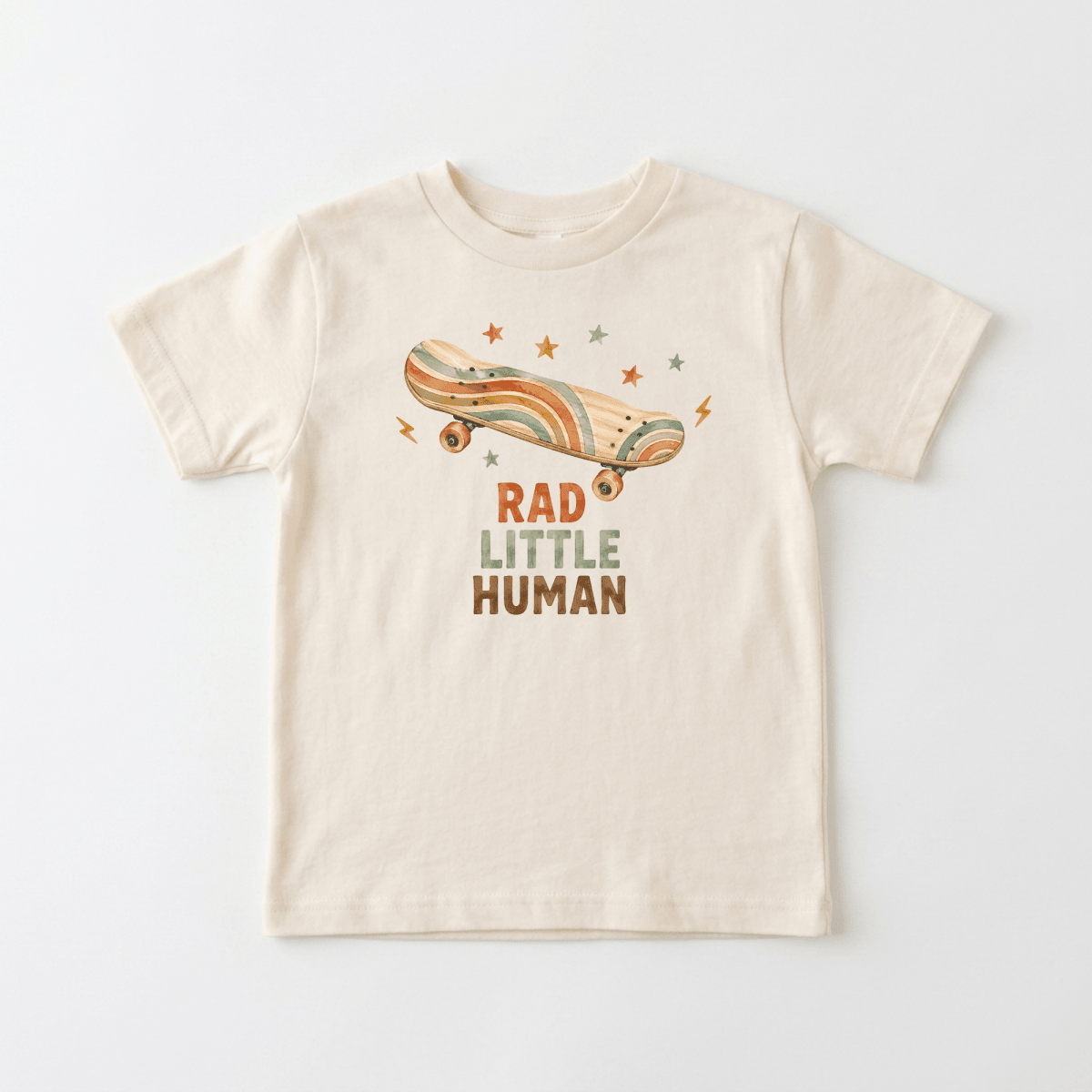 Introducing the Toddler Skateboard Shirt – Rad Little Human Short-Sleeve Graphic Tee by Toodleroos. This beige skater shirt features a vintage-style skateboard, stars, and lightning bolts above the bold RAD LITTLE HUMAN text. Set against a plain white background, this retro toddler graphic tee is perfect for your little one with standout style.