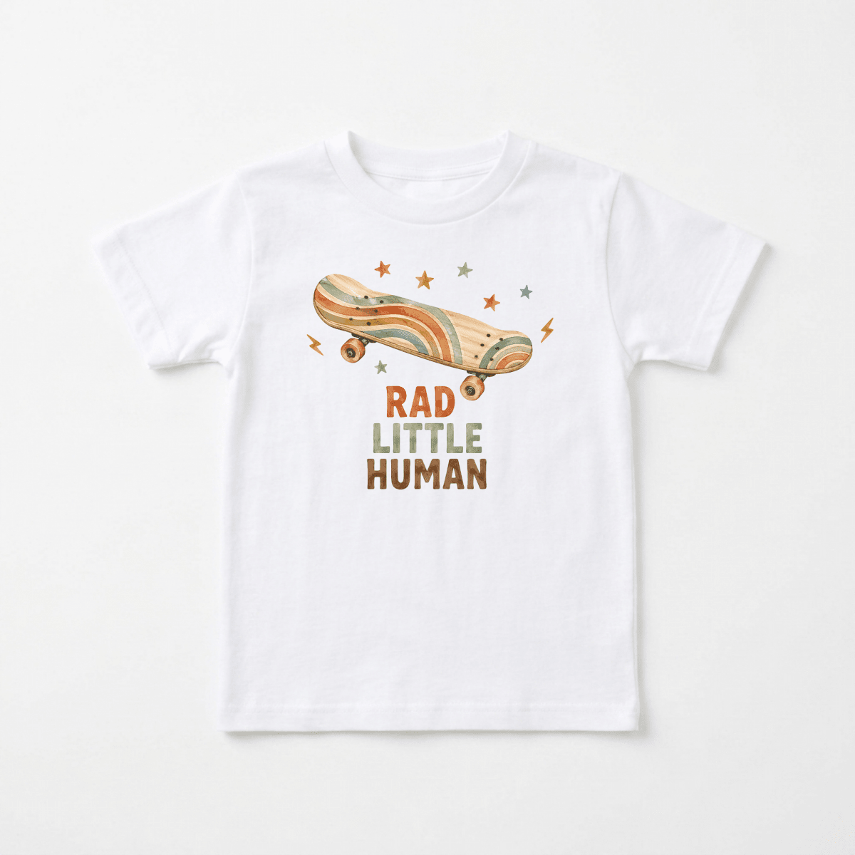 Dress your little one in standout style with the Toodleroos Toddler Skateboard Shirt – Rad Little Human Short-Sleeve Graphic Tee. This white children’s t-shirt showcases a retro-style skateboard adorned with stars and lightning bolts above the bold, colorful text “RAD LITTLE HUMAN.” Perfect for toddlers who love cool, vintage-inspired fashion!.