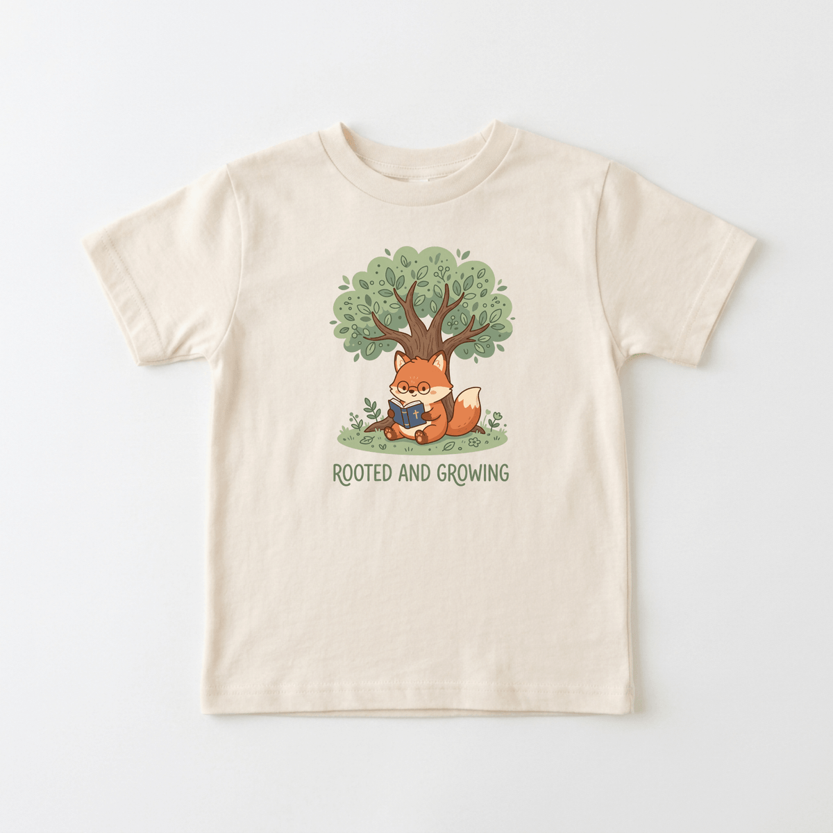 The Rooted and Growing Fox Kids Shirt – Faith Tee by Toodleroos is a cream t-shirt showcasing a charming illustration of a fox reading beneath a leafy tree with visible roots. Beneath the artwork, the phrase “ROOTED AND GROWING” is displayed. This faith-inspired kids’ shirt from Toodleroos is perfect for little ones who love animal designs and gentle Christian messages.