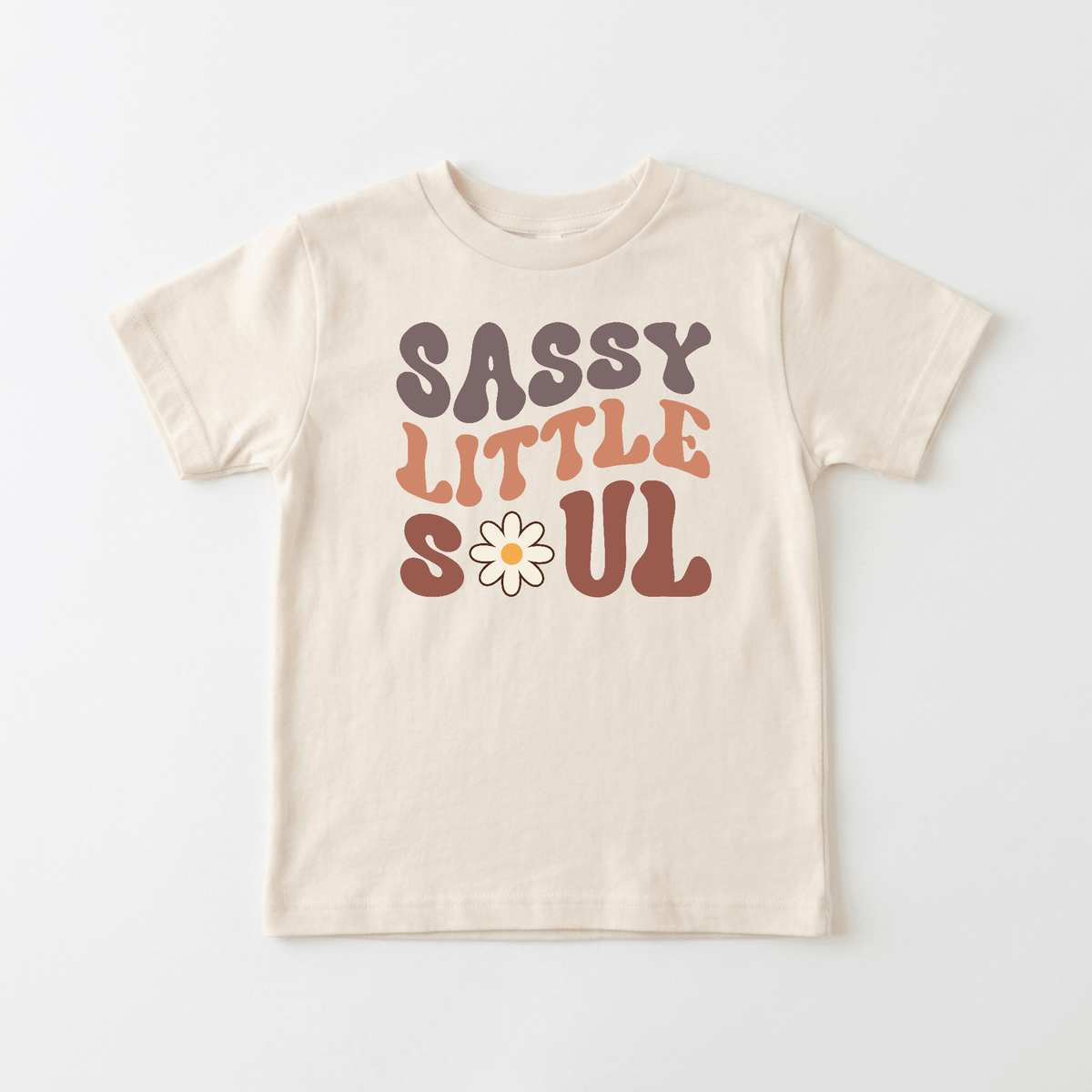 The Sassy Little Soul Kids Shirt – Boho Retro Tee from Toodleroos features bold, retro-inspired “Sassy Little Soul” lettering in purple, orange, and brown, with a daisy as the O in “Soul.” This beige t-shirt is an effortlessly fun boho kids’ shirt—perfect for showing off your little one’s sassy personality.