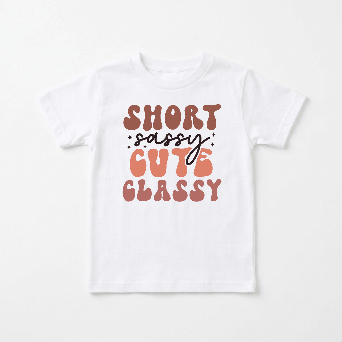 The Short Sassy Cute Classy Kids Shirt – Retro Tee from Toodleroos features stylized brown and peach text that reads “Short Sassy Cute Classy,” accented with small stars around “sassy.” This retro kids’ shirt adds a playful, vintage flair to any outfit.