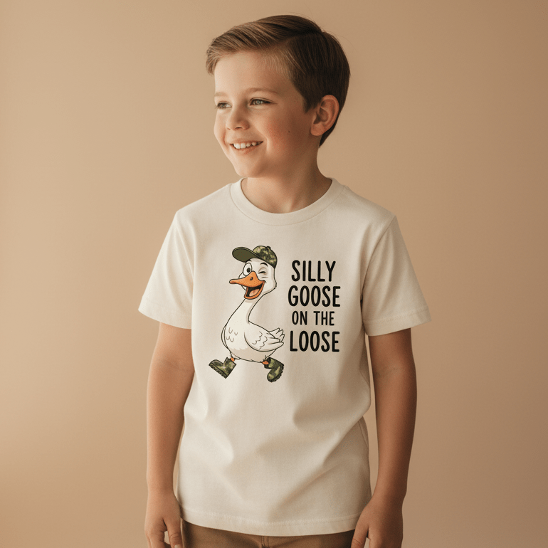 A cheerful boy wears the Toodleroos Silly Goose on the Loose Toddler Shirt – a fun kids animal tee featuring a cartoon goose in a cap and boots, with quirky “Silly Goose on the Loose” text. This funny toddler shirt is perfect for little ones who love playful styles.