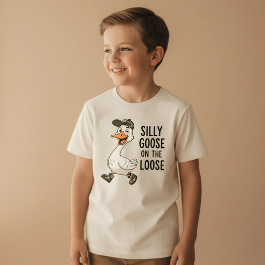 A cheerful boy wears the Toodleroos Silly Goose on the Loose Toddler Shirt – a fun kids animal tee featuring a cartoon goose in a cap and boots, with quirky “Silly Goose on the Loose” text. This funny toddler shirt is perfect for little ones who love playful styles.