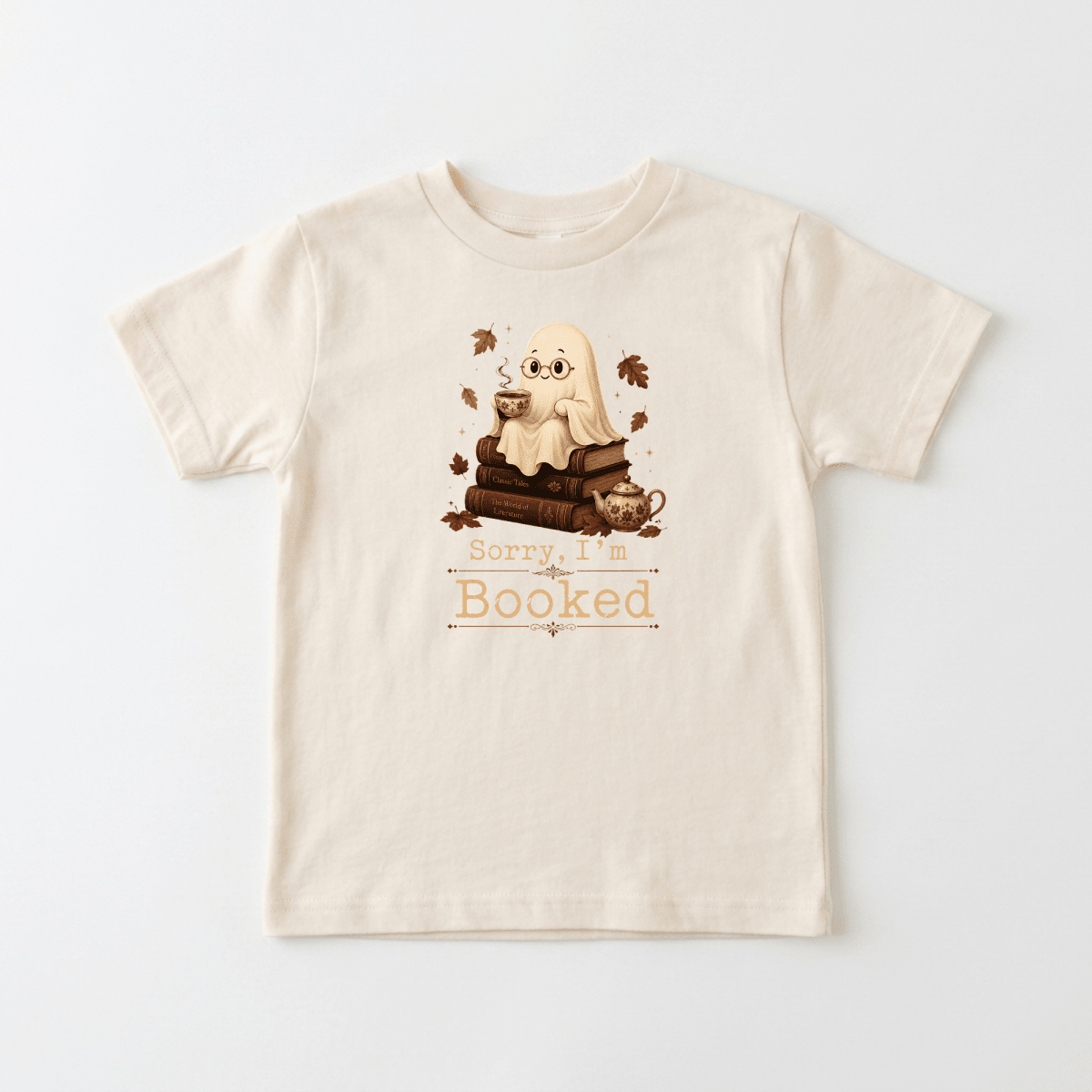 Dress your little bookworm in the Toodleroos “Sorry I’m Booked Toddler Shirt – Cozy Ghost Reading Tee.” This adorable beige Halloween kids shirt features a charming ghost holding a mug, perched on a stack of books surrounded by autumn leaves. With the playful phrase “Sorry, I’m Booked” beneath the design, it’s perfect for cozy reading days and fall festivities.