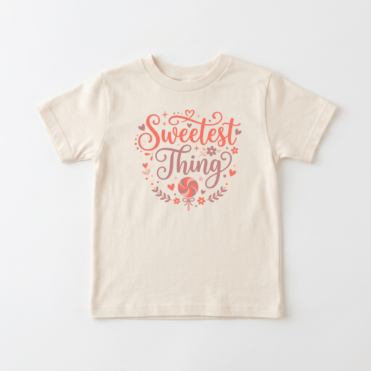The Toodleroos Sweetest Thing Toddler Girls Shirt – Floral Lollipop Tee features a cream-colored design with pink and red decorative text reading “Sweetest Thing,” surrounded by playful hearts, flowers, and swirls—perfect for fans of cute kids shirts.